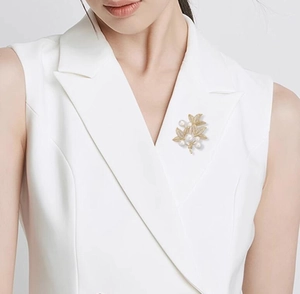 Detail of a luxury gold leaf brooch with white pearls pinned on a white vest lapel