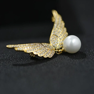 Détail d'une broche aile d'ange dorée sertie de cristaux avec une perle pendante