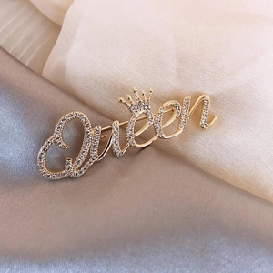 Makroaufnahme der vergoldeten Queen-Buchstaben-Brosche mit Krone und Kristallen