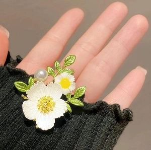Elegante Gänseblümchen-Brosche mit weißen Blüten, gelben Staubfäden und Perle auf Stoff