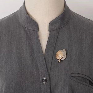 Detailed view of layered maple leaf brooch with pearl on a grey shirt collar