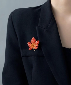 Detailed close-up of a vibrant red maple leaf brooch pinned on a black business suit blazer