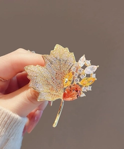 Close-up of vintage hollow maple leaf brooch with sparkling crystals and golden finish