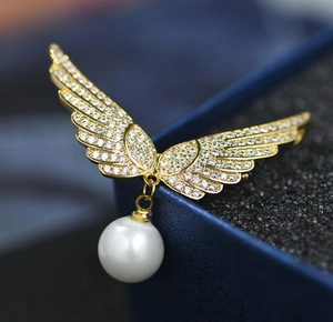 Détail de la broche aile d'ange avec strass brillants et une perle blanche suspendue