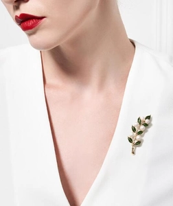Élégante broche feuille en or avec émail vert et perles portée sur un col en V blanc