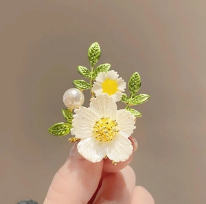 Detaillierte Nahaufnahme einer Gänseblümchen-Brosche mit weißen Blütenblättern und Blättern