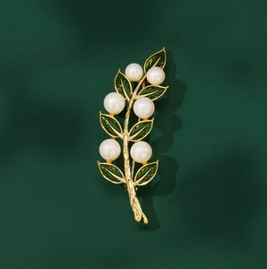 Élégante broche feuille dorée avec émail vert et perles blanches sur fond sombre