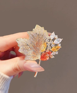 Close-up of a maple leaf brooch with golden metal and sparkling orange crystals