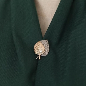 Macro detail of leaf brooch with gold and silver layered textures and a small white pearl