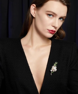 Détail d'une broche fleur de luxe avec perle, diamants et émail vert sur un blazer noir chic