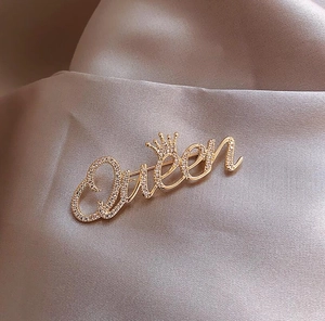 Detailansicht der goldenen Queen-Brosche mit Strasssteinen auf Satin-Hintergrund