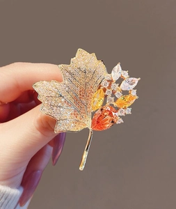 Detail of vintage gold maple leaf brooch with vibrant orange crystals on hand