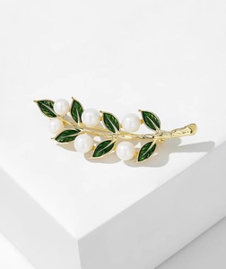 Élégante broche feuille dorée avec perles blanches et émail vert sur un socle blanc