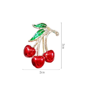 Detail view of a 3x2cm red cherry brooch with gold accents and green enamel leaves