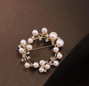 Detail of a floral circular brooch with golden alloy base, pearls and sparkling zircons
