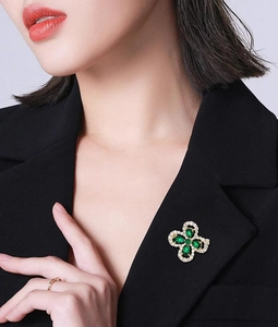 Détail d'une broche trèfle vintage en émeraude sur le revers d'un blazer noir