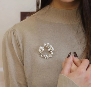 Close-up of elegant pearl wreath brooch on a khaki knit sweater with golden metal details