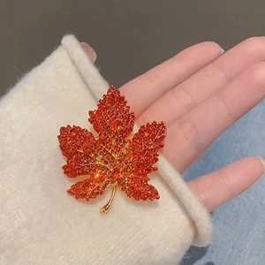 Elegant maple leaf brooch with orange crystals on gold metal shown on a white sweater
