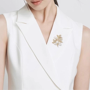 Elegant gold leaf brooch with white pearls and sparkling zircons on white blazer