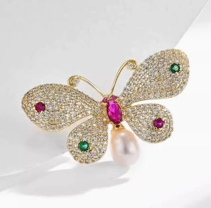 Macro detail of butterfly brooch with colorful crystals and a teardrop pearl pendant