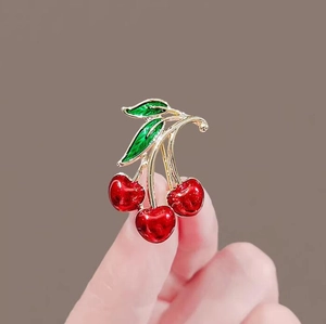 Exquisite red cherry brooch with green leaves and gold metal plating held by hand