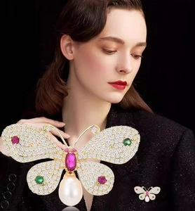Detailed view of luxury gold butterfly brooch with colorful crystals and pearl drop on coat