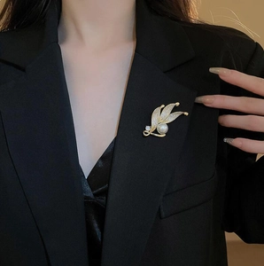 Eleganter Goldblatt-Anstecker mit Kristallen und Perle an einem schwarzen Blazer
