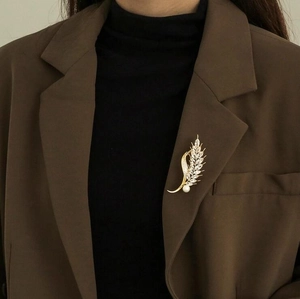 Elegant wheat ear brooch with gold metal, sparkling zircons, and white pearl on a blazer