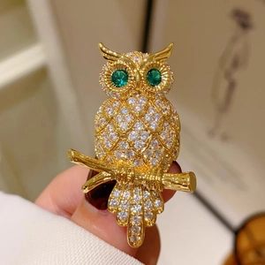 Funkelnde goldene Eulenbrosche mit weißen Kristallen und grünen Steinaugen am Ast