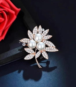 Close-up of pearl flower brooch with white rhinestones on rose gold base near a red rose