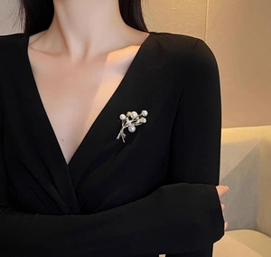 Dettaglio di una spilla di lusso con perle e spighe indossata su un abito nero elegante