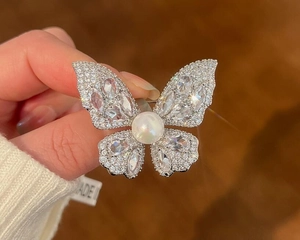 Macro shot of sparkling butterfly brooch with white rhinestones and large pearl center