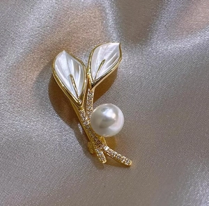 Vue macro d'une broche feuille dorée avec perle blanche, nacre et accents de zircon