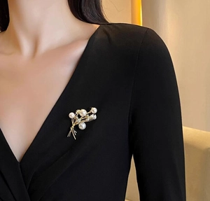 Elegante spilla a spiga di grano dorata con perle e cristalli su un abito nero