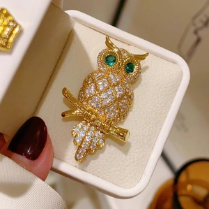 Makroaufnahme der goldenen Eulenbrosche mit weißen Diamanten und smaragdgrünen Augen