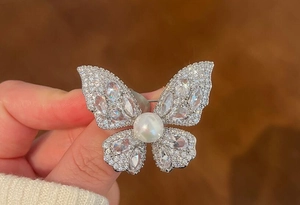 Close-up of sparkling butterfly brooch with pavé rhinestones and a large white pearl