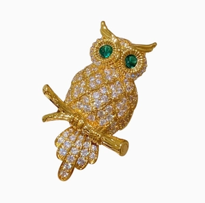 Goldene Eulenbrosche mit weißen Zirkonia und grünen Edelsteinaugen auf weißem Grund