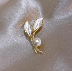 Vue macro d'une broche perle en forme de feuille avec base dorée sur tissu satin