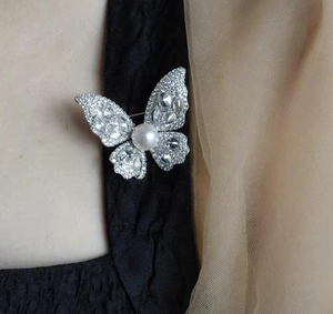 Detailed close-up of butterfly brooch with sparkling crystals and a large white pearl