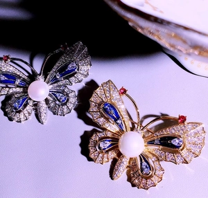 Gros plan de broches papillon en or et argent avec perles et détails en émail bleu clair