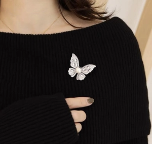 Detailed close-up of butterfly brooch with sparkling crystals and a pearl on a black knit