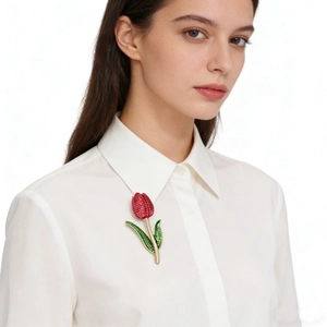 Close-up of a tulip flower brooch with red enamel and gold alloy on a white shirt