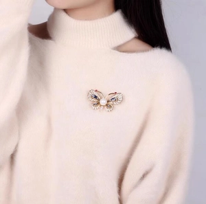 Broche papillon élégante avec perle et cristaux sur un pull beige doux