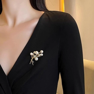 Elegante spilla a spiga con perle e strass dorati su un top nero con scollo a V