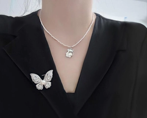 Close-up of a sparkling butterfly brooch and pearl necklace on a black blazer