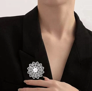 Détail d'une broche fleur argentée avec perles et strass portée sur une veste noire