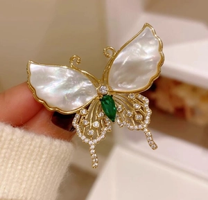 Detalle macro de broche de mariposa vintage con nácar y piedra preciosa verde