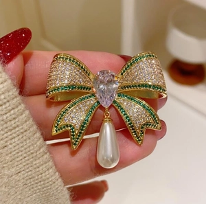 Close-up of a sparkling bow brooch with green stones and a white teardrop pearl
