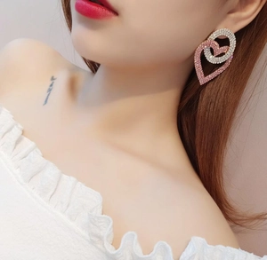Detail of interlocking pink and white crystal heart earrings worn by a model