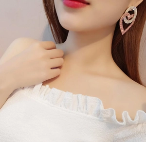 Detail of pink and white crystal heart earrings worn by a model with a shimmering finish